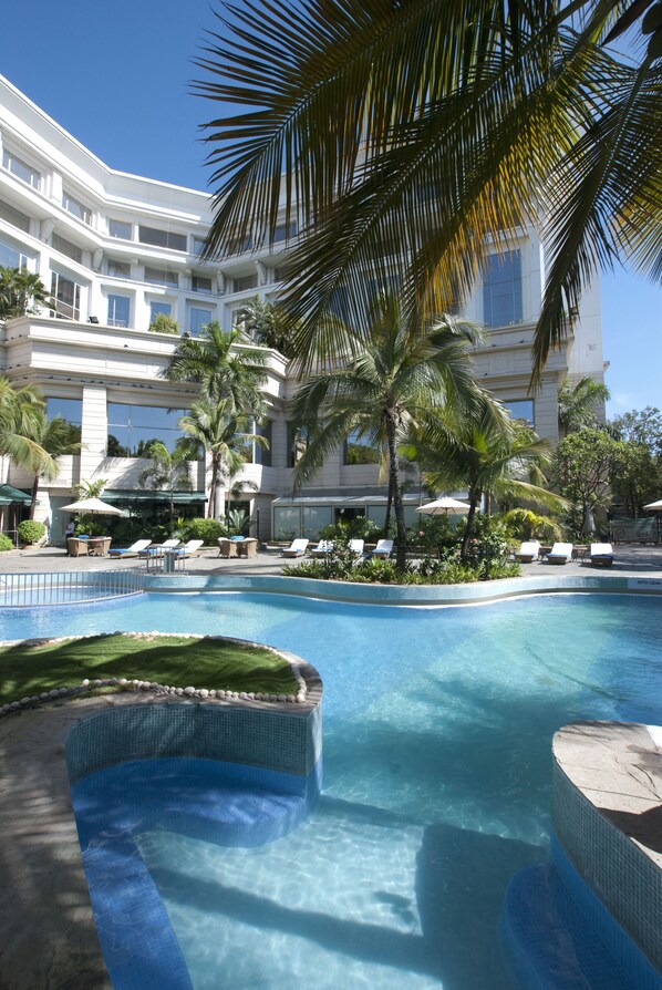 A swimming pool with lounge chairs and palm trees, surrounded by a building with multiple balconies. - ITC Kakatiya, a Luxury Collection Hotel, Hyderabad (Hyderabad)