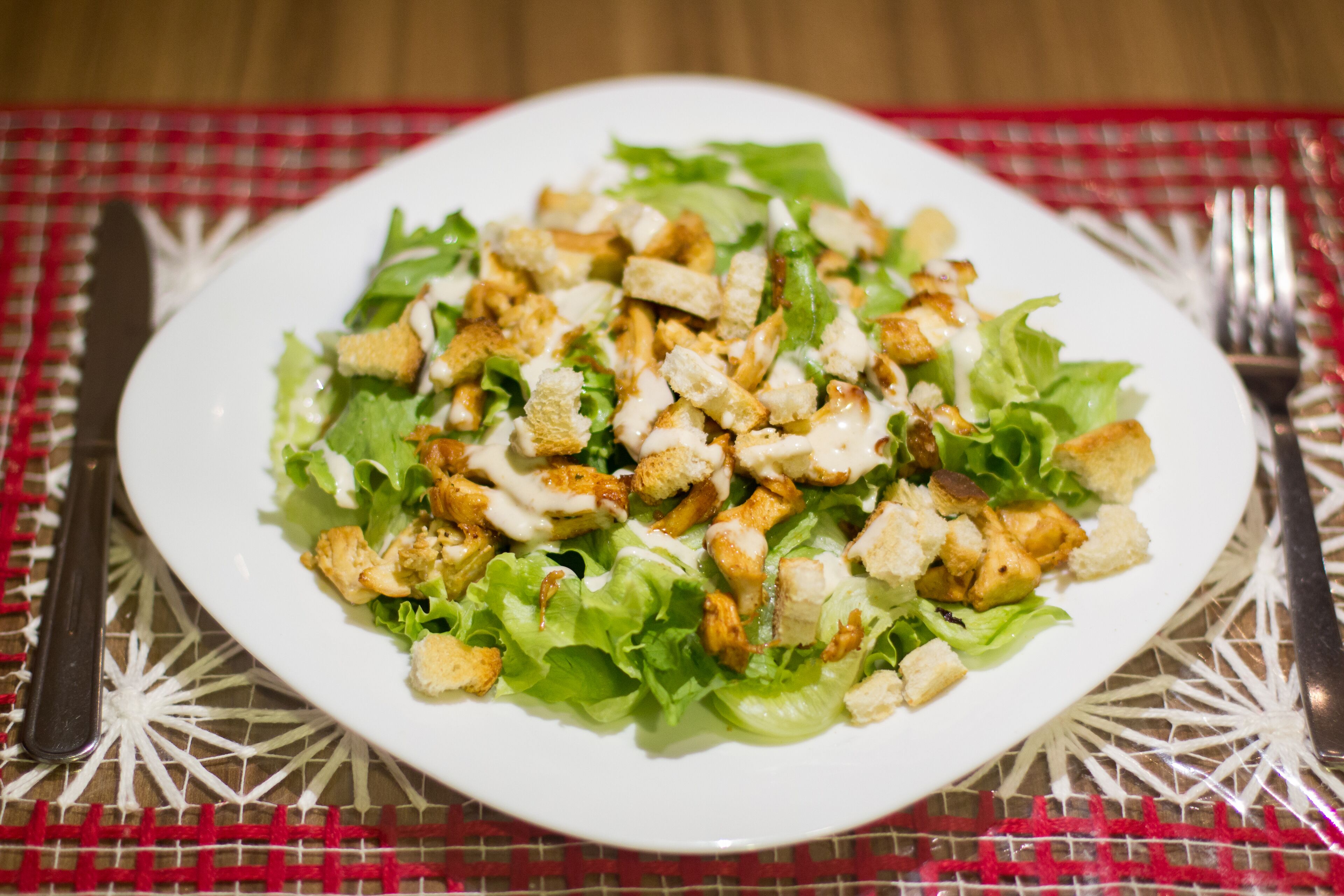 A plate of salad with croutons and a white plate on a table with a red and white checkered tablecloth.