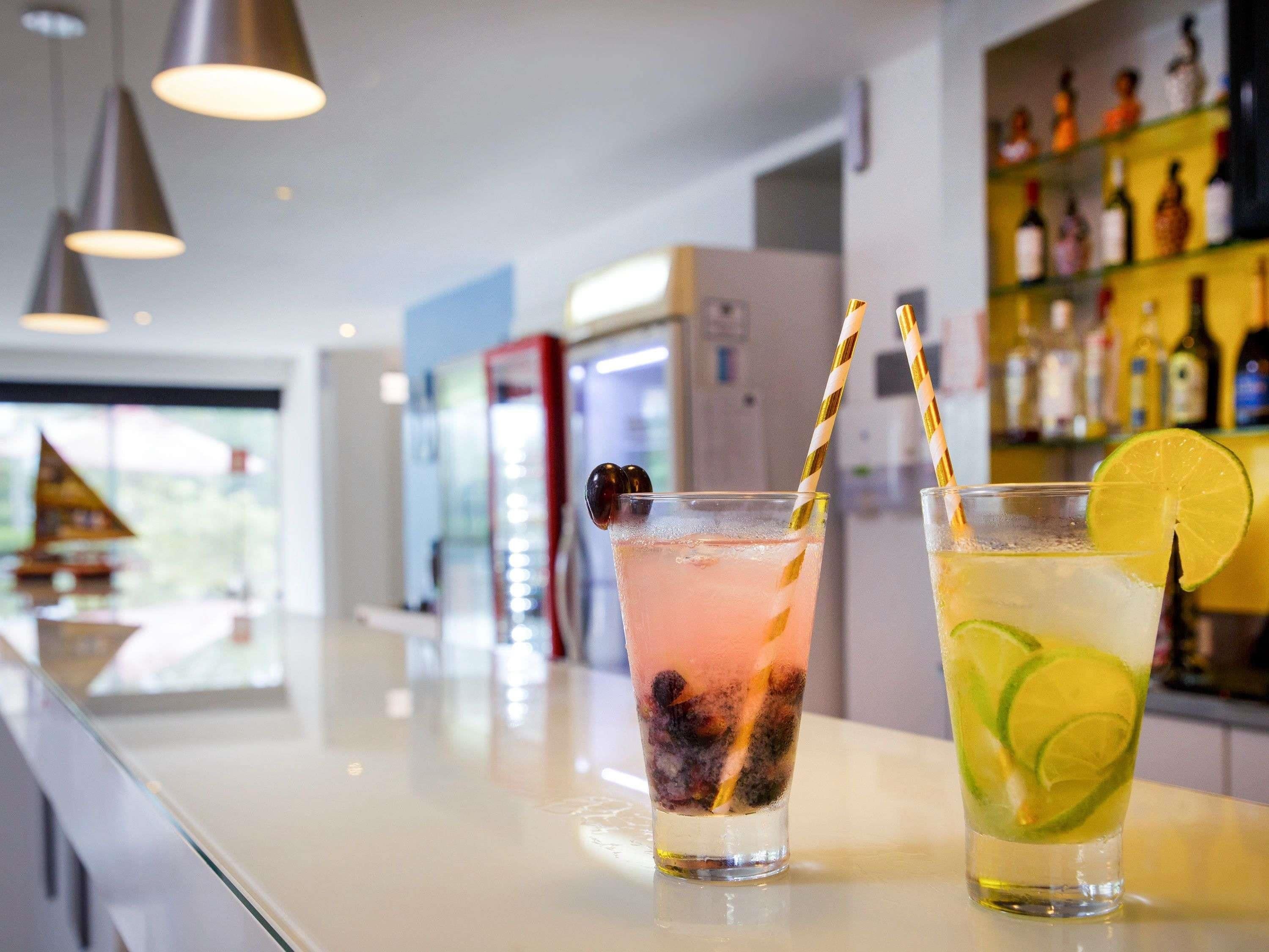 Two drinks on a bar counter with a view of a ship model and a shelf of bottles in the background.