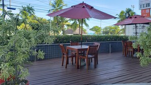 A wooden deck with a table and chairs, surrounded by potted plants and umbrellas. - Ibis Maceio Pajucara (Maceió)