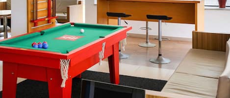 A pool table with balls, a laptop, and a bar area with stools.