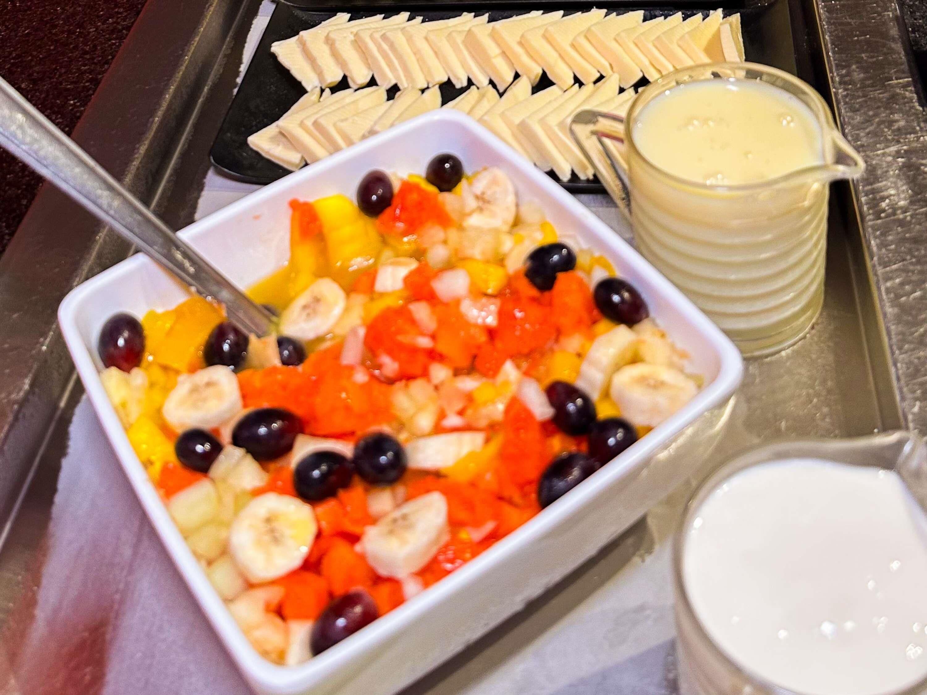 Un plateau avec un saladier de salade de fruits, un verre de lait et des bananes coupées en tranches.