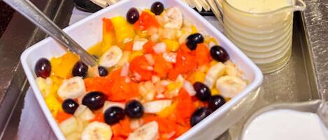 Un plateau avec un saladier de salade de fruits, un verre de lait et des bananes coupées en tranches.