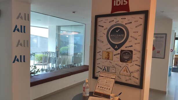 A modern interior with a large window, a framed artwork with the word "ACCORD" repeated, and a sign with COVID-19 guidelines. - Ibis Maceio Pajucara (Maceió)