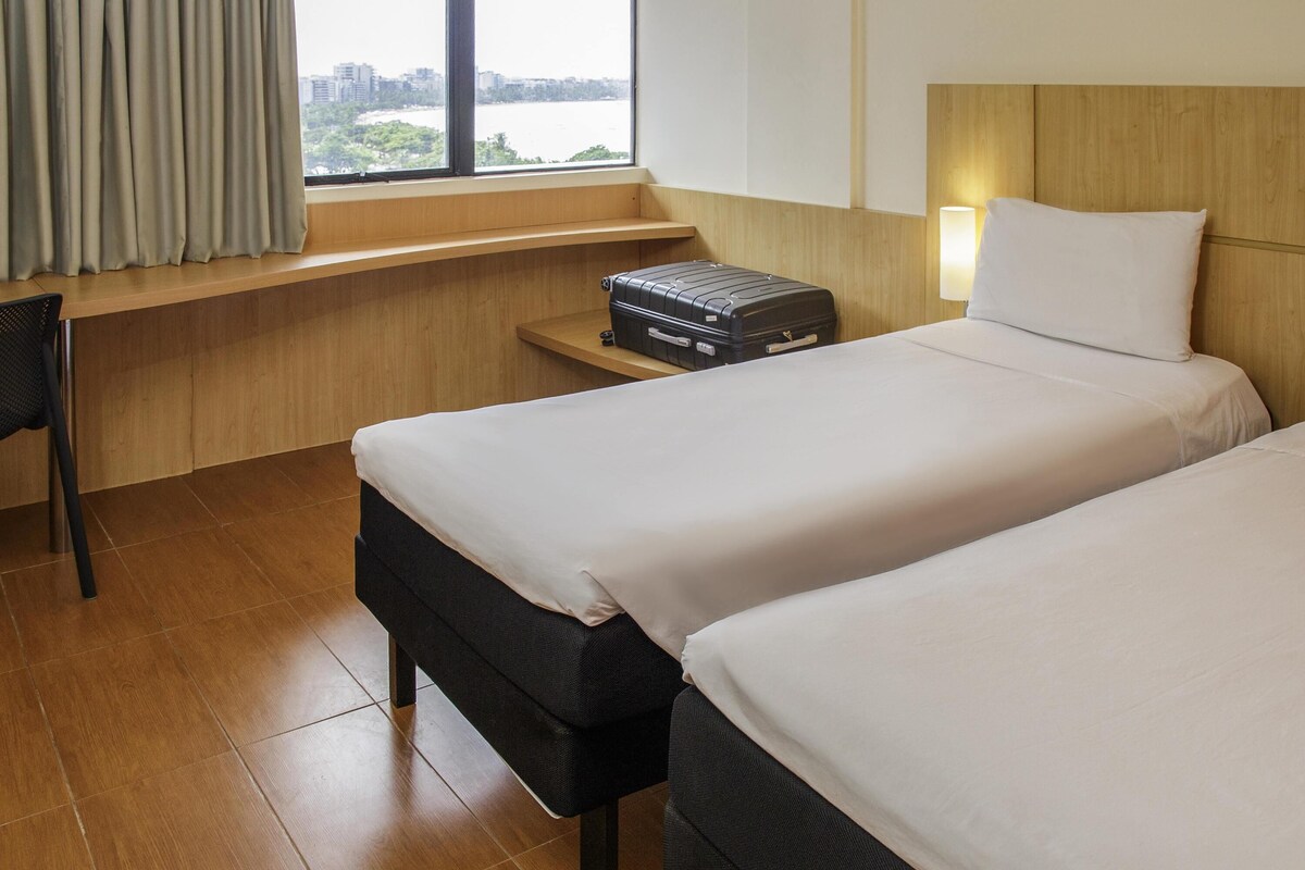 A hotel room with two beds, a desk, a suitcase, and a view of a body of water.