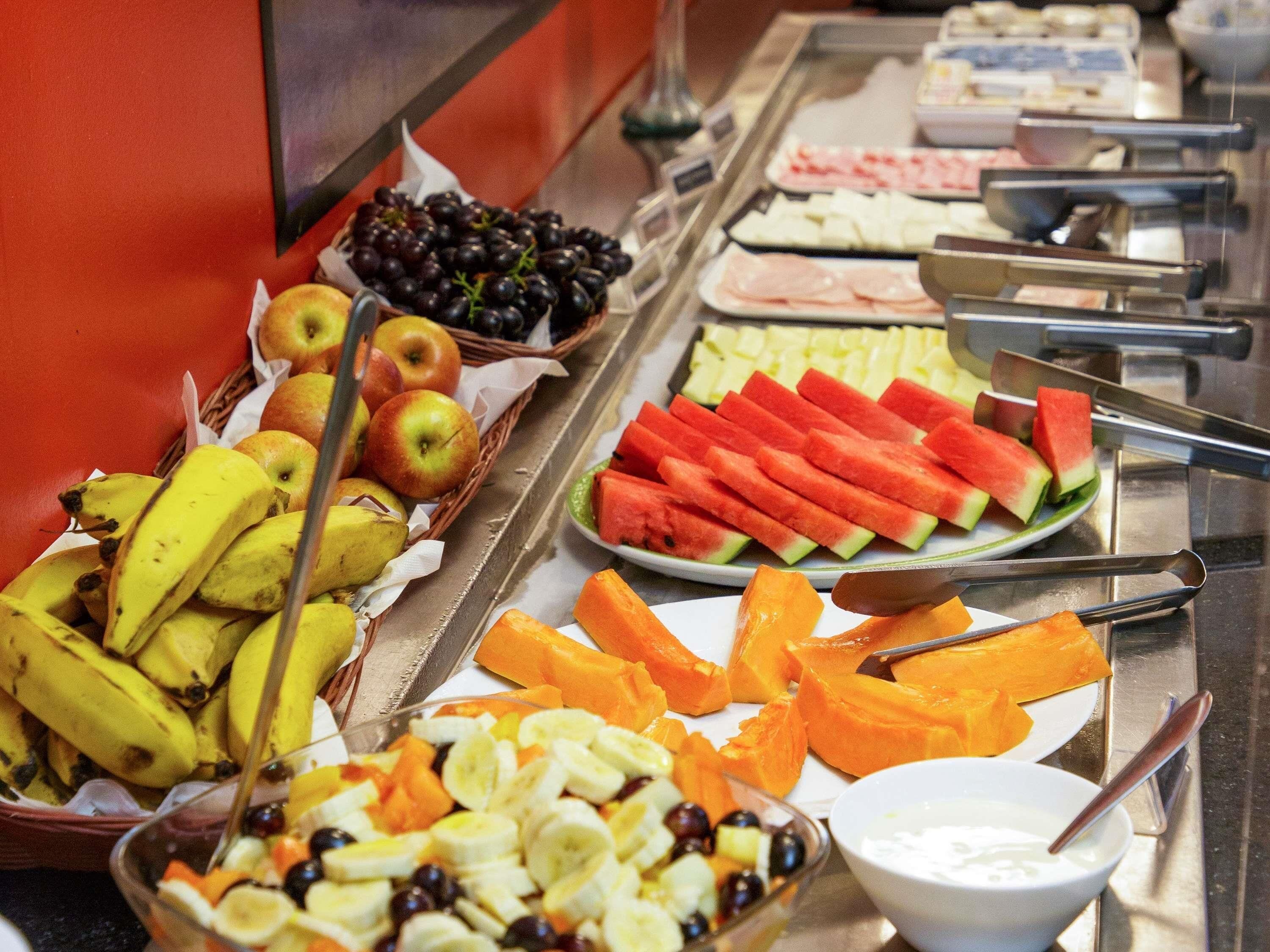 Un buffet proposant une variété de fruits et de légumes, notamment des bananes, des pommes, des pastèques et des carottes.