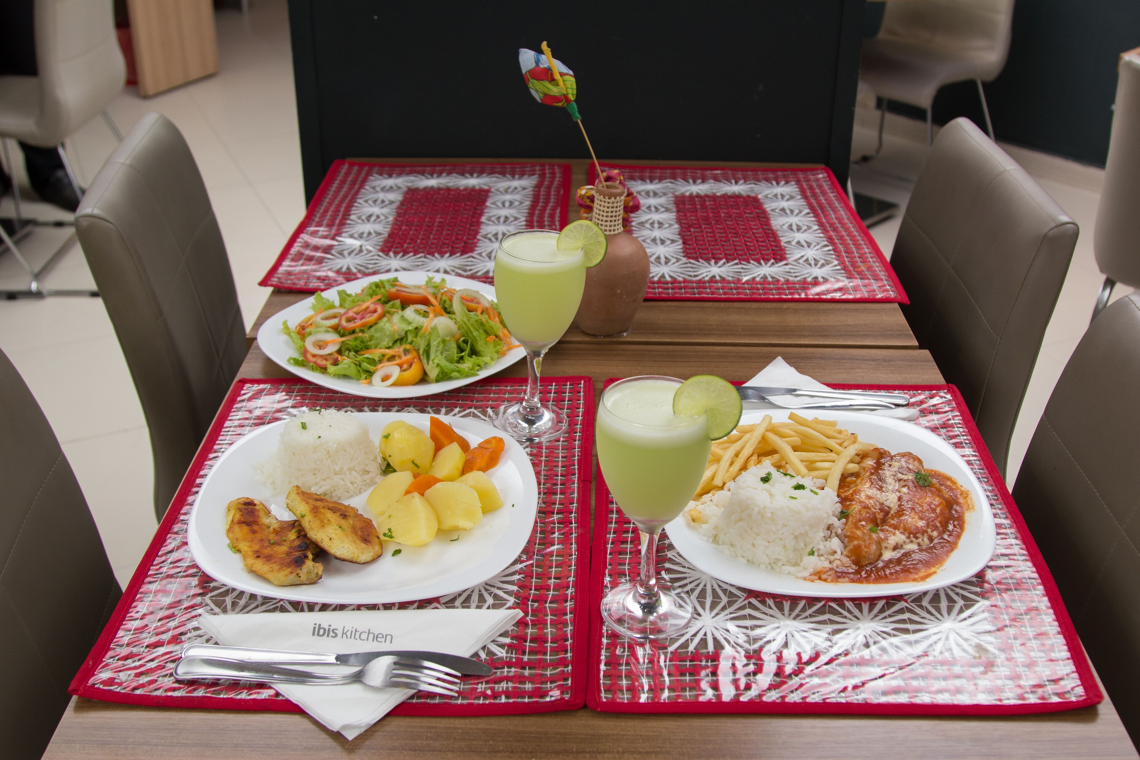 Une table dressée avec des assiettes remplies de nourriture, notamment du riz, du poulet et une salade, ainsi qu'un verre d'une boisson verte.