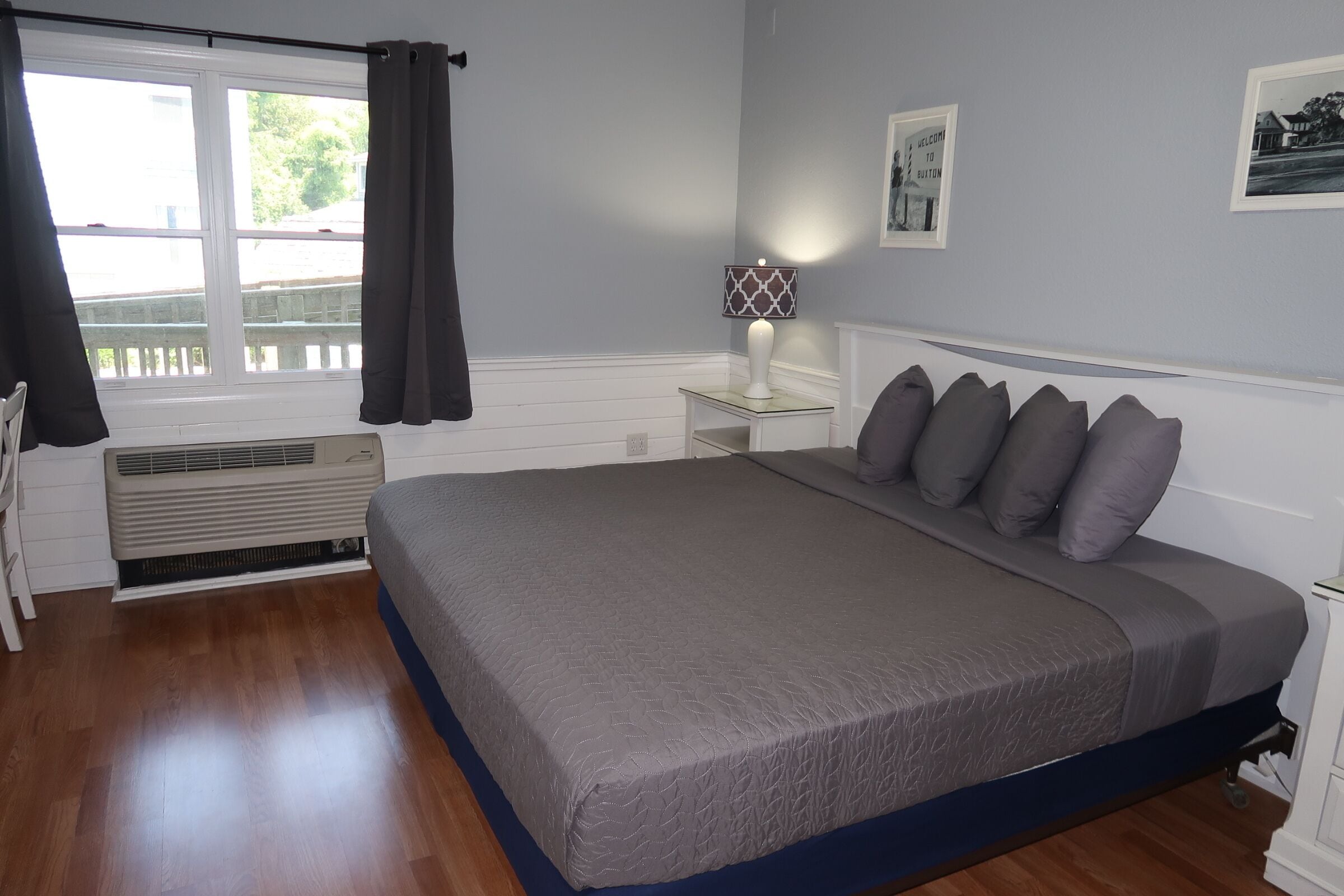 A bedroom with a large bed, a bedside table with a lamp, a window with curtains, and a radiator.