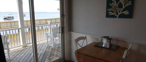 A room with a wooden table and chairs, a sliding glass door leading to a balcony with a view of the sea and boats.