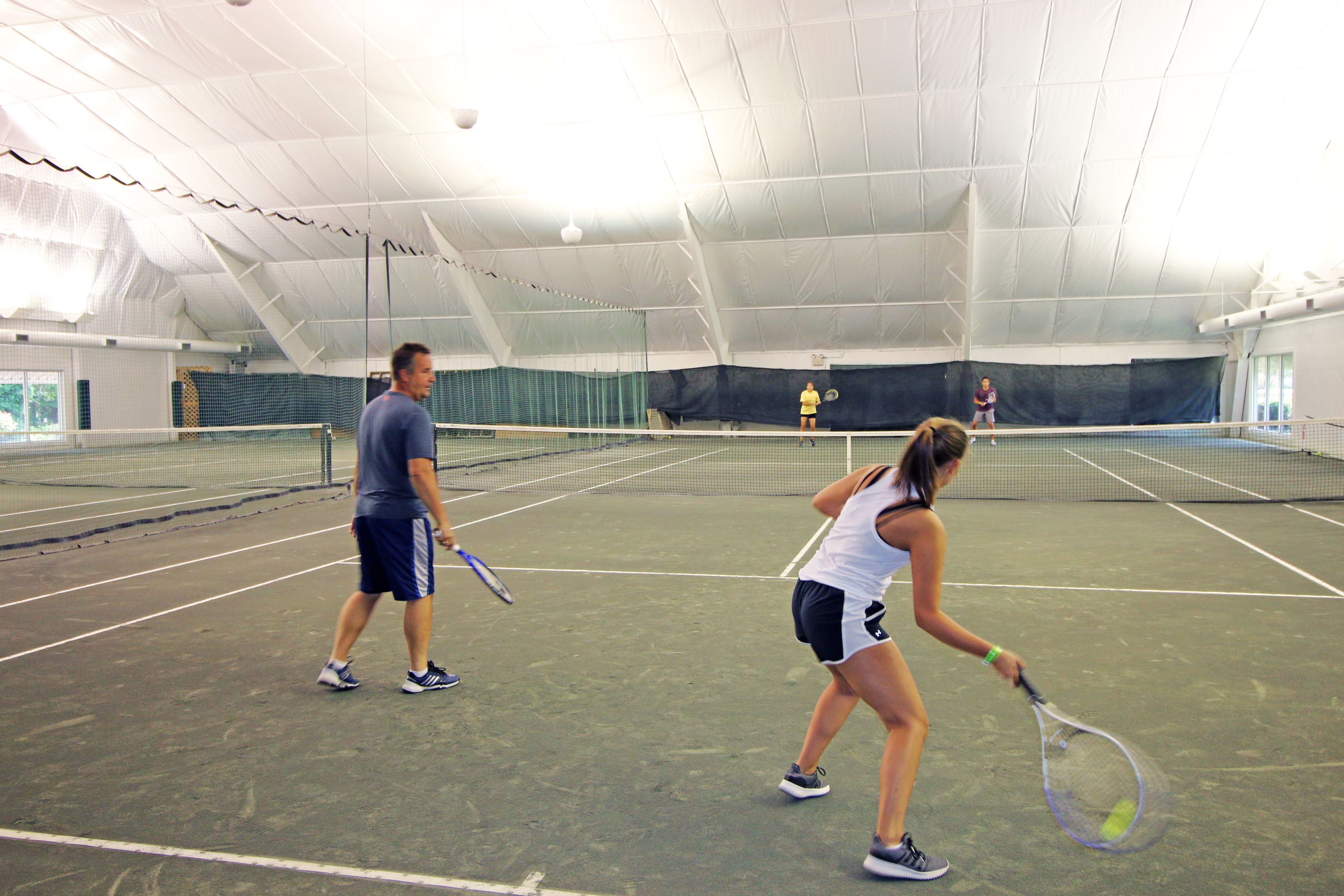 An indoor tennis court with a net, a man and a woman practicing.