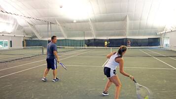 An indoor tennis court with a net, a man and a woman practicing.