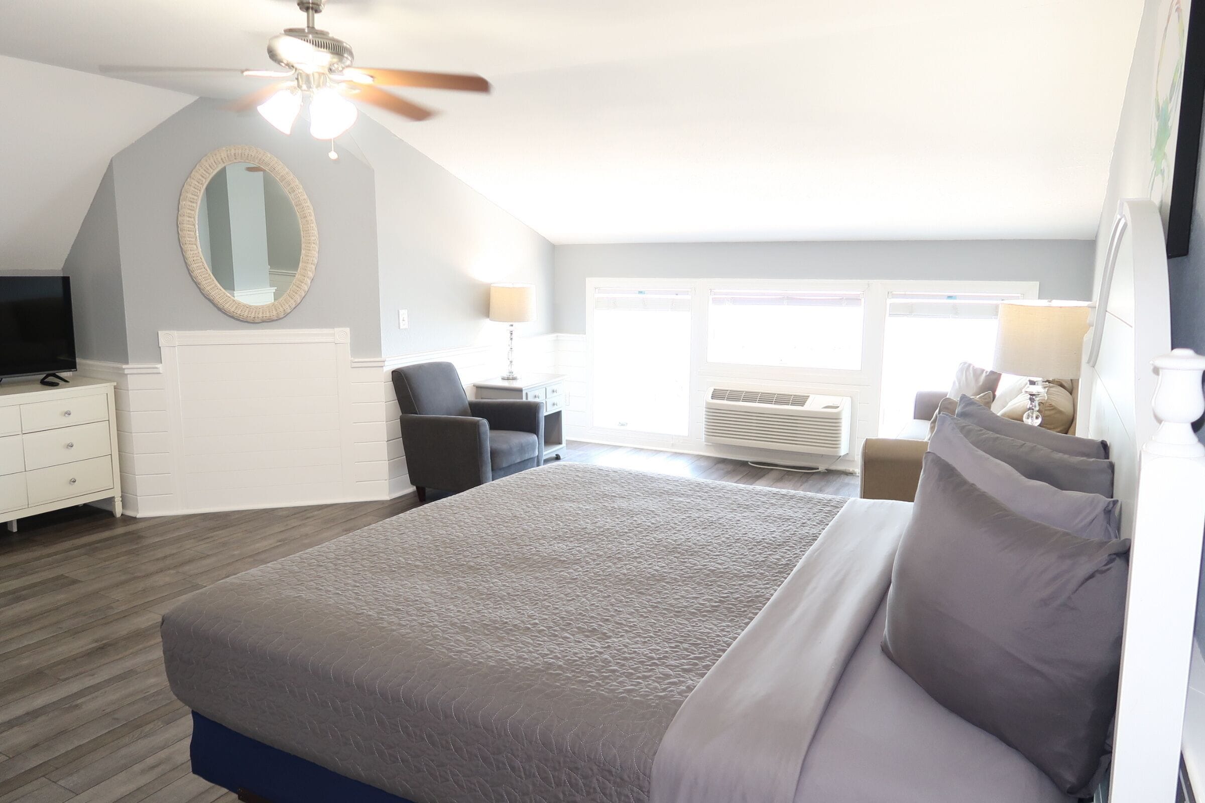 A bedroom with a bed, a desk, a chair, a mirror, and a ceiling fan.