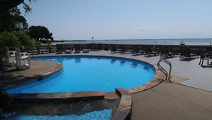 Une piscine entourée d’arbres, avec une terrasse en bois et des chaises longues, offrant une vue sur la mer.