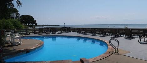 Una piscina con muelle de madera y sillas de descanso, rodeada de árboles y vistas al mar.
