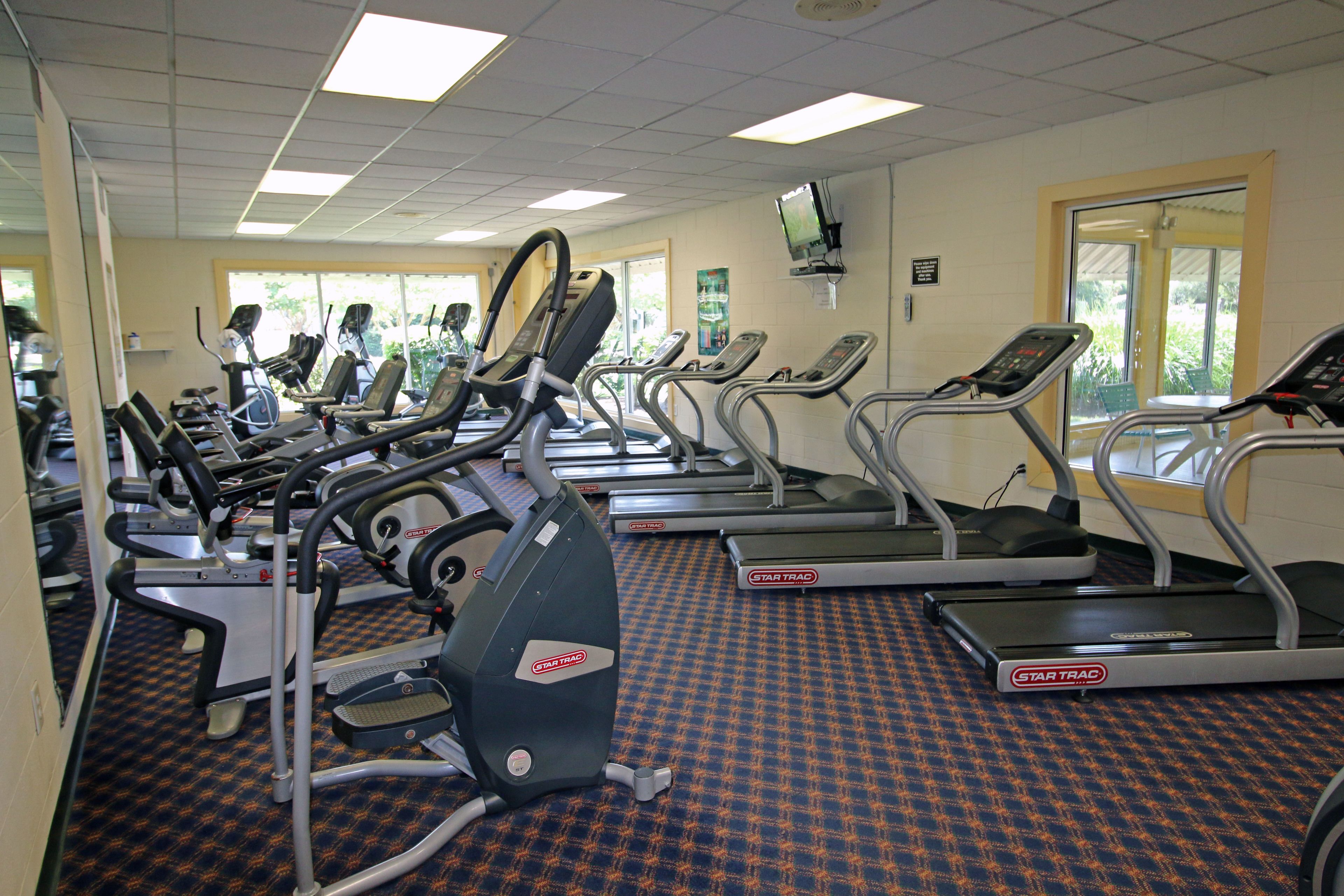 A gym with treadmills and elliptical machines, a patterned carpet, and a television on the wall.