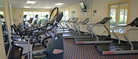 A gym with treadmills and elliptical machines, a patterned carpet, and a television on the wall.