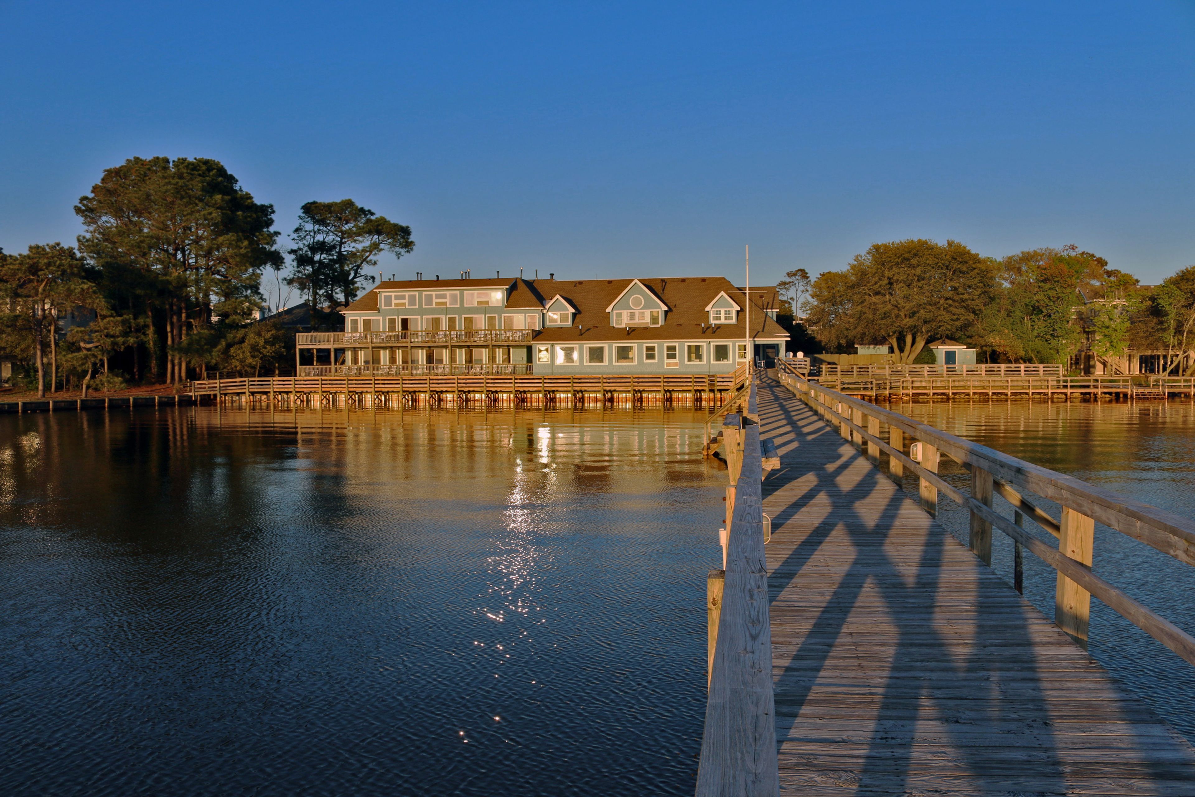 A waterfront property with a wooden deck leading to a house with multiple windows and a balcony.