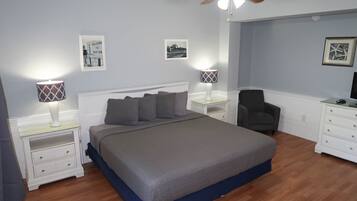Une chambre à coucher comprenant un lit, des tables de chevet, une chaise, une commode et un ventilateur de plafond.