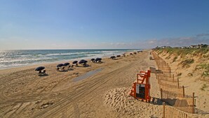 A sandy beach with a wooden fence, beach umbrellas, and a lifeguard tower. - The Inn At Corolla Light (Corolla)
