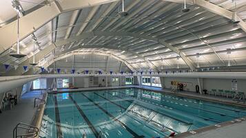 An indoor swimming pool with multiple lanes, safety railings, and a high, arched ceiling.