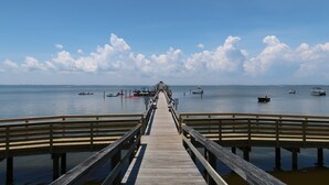 Une jetée en bois s’étendant sur une étendue d’eau calme, avec des bateaux et un ciel dégagé.