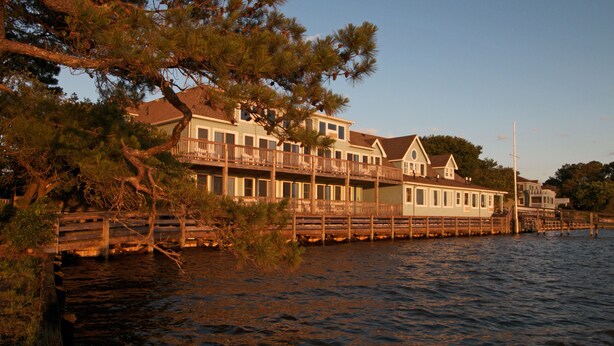 A waterfront property with a multi-story building, a dock, and a wooden bridge. - The Inn At Corolla Light (Corolla)