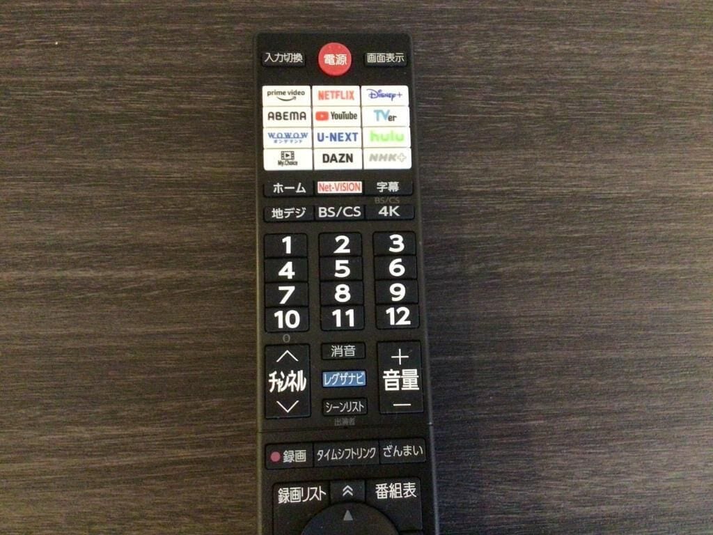 Un control remoto con varios botones y etiquetas, incluyendo logotipos de marcas y texto en japonés.