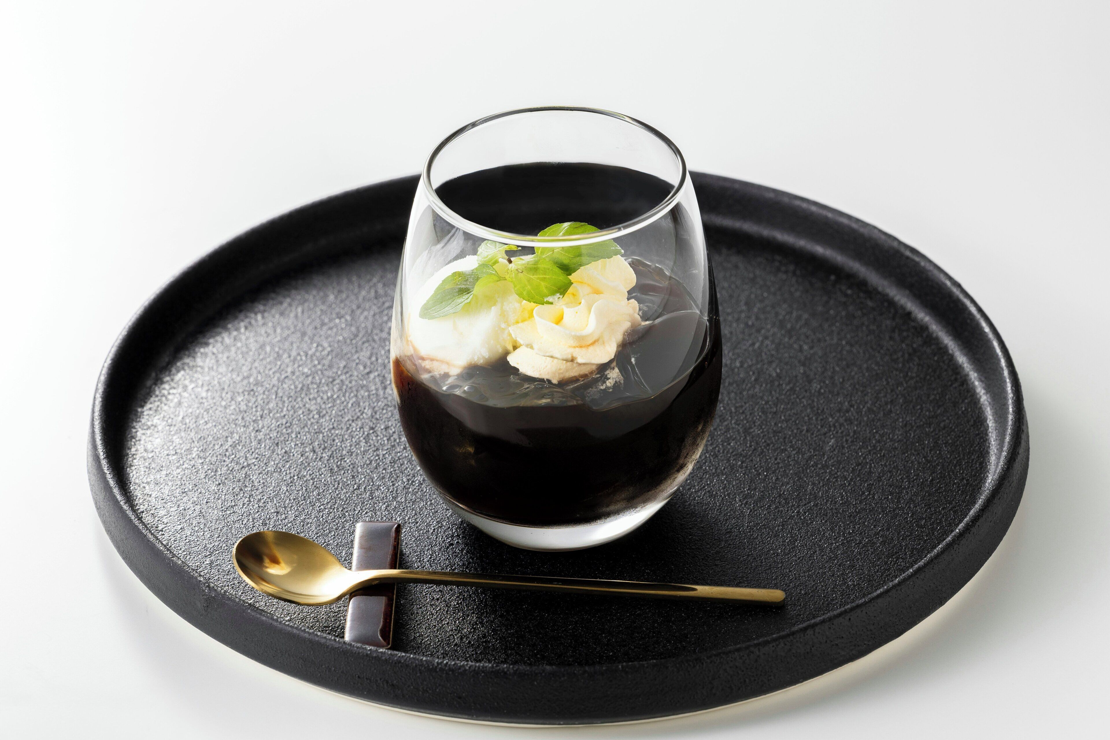 Un postre en un vaso sobre un plato negro, con una cuchara al lado.