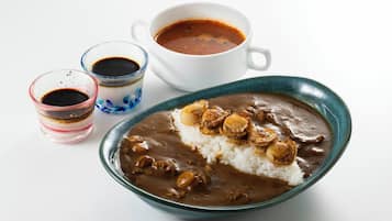 Un tazón de curry con arroz y cebollas fritas, acompañado por dos vasos pequeños de salsa y una taza de té.