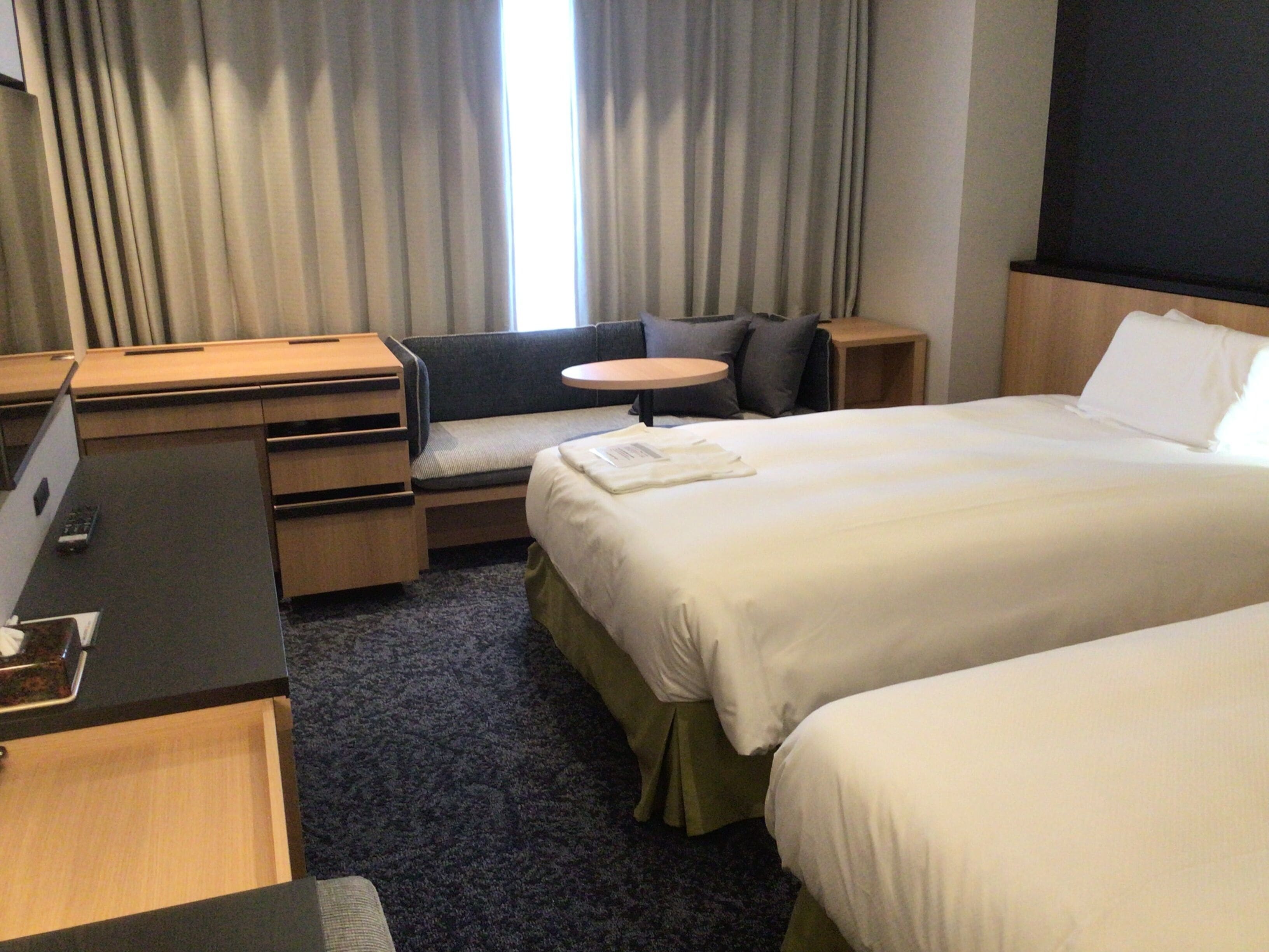 A hotel room with a bed, a desk, a chair, and a small table.