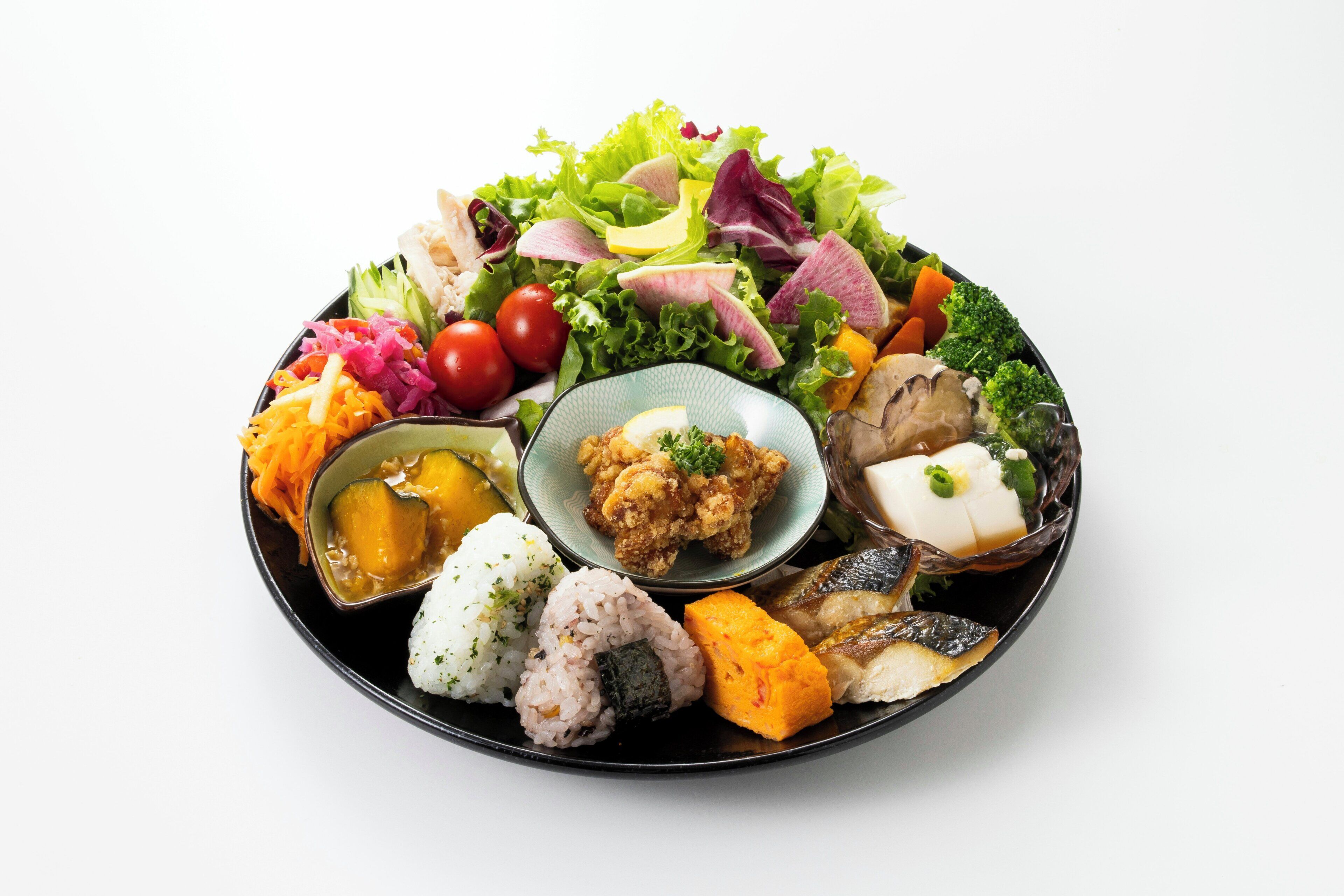 Un plato redondo negro con diferentes alimentos, como arroz, verduras y una ensalada.