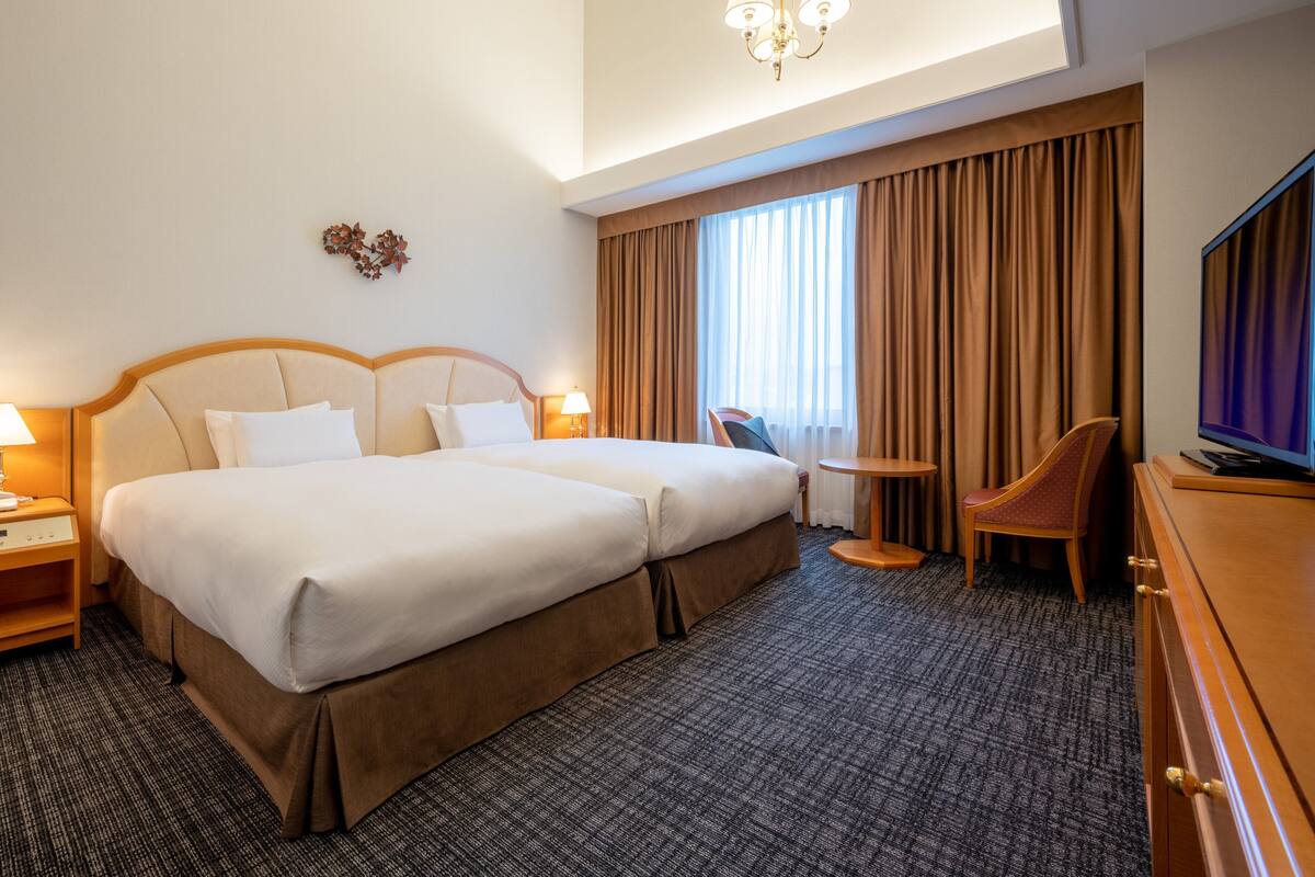 A hotel room with a double bed, a small table, a TV, and a chair.