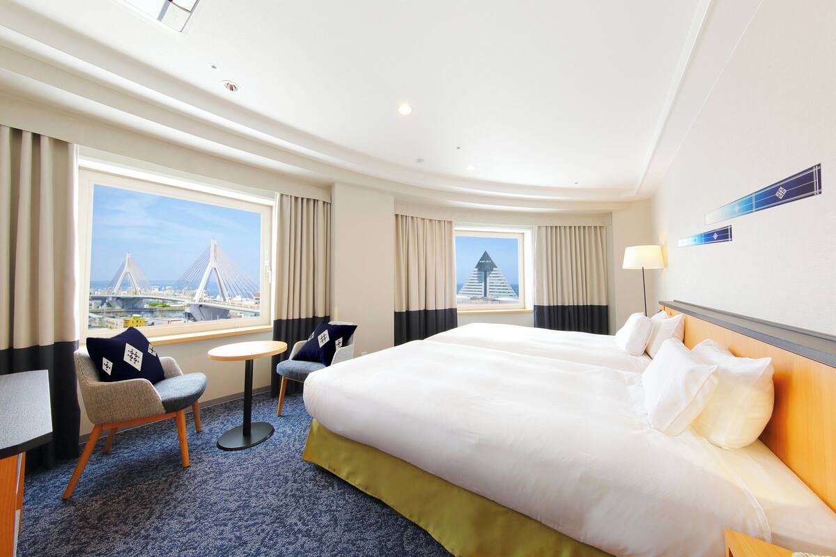 A hotel room with a large bed, a desk, a chair, and a view of a bridge.