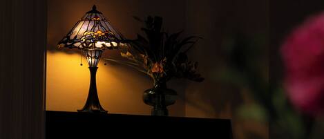 A table lamp with a stained glass shade and a vase with flowers on a table against a wall.