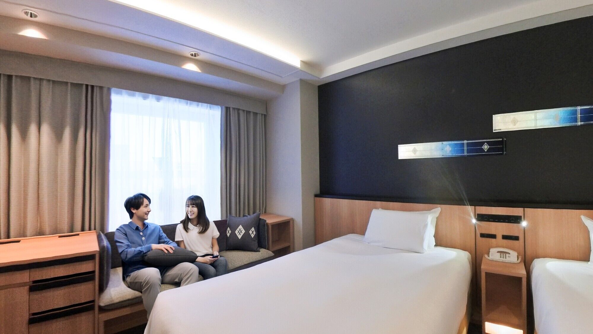 A hotel room with a large bed, a desk, and a seating area with two people.
