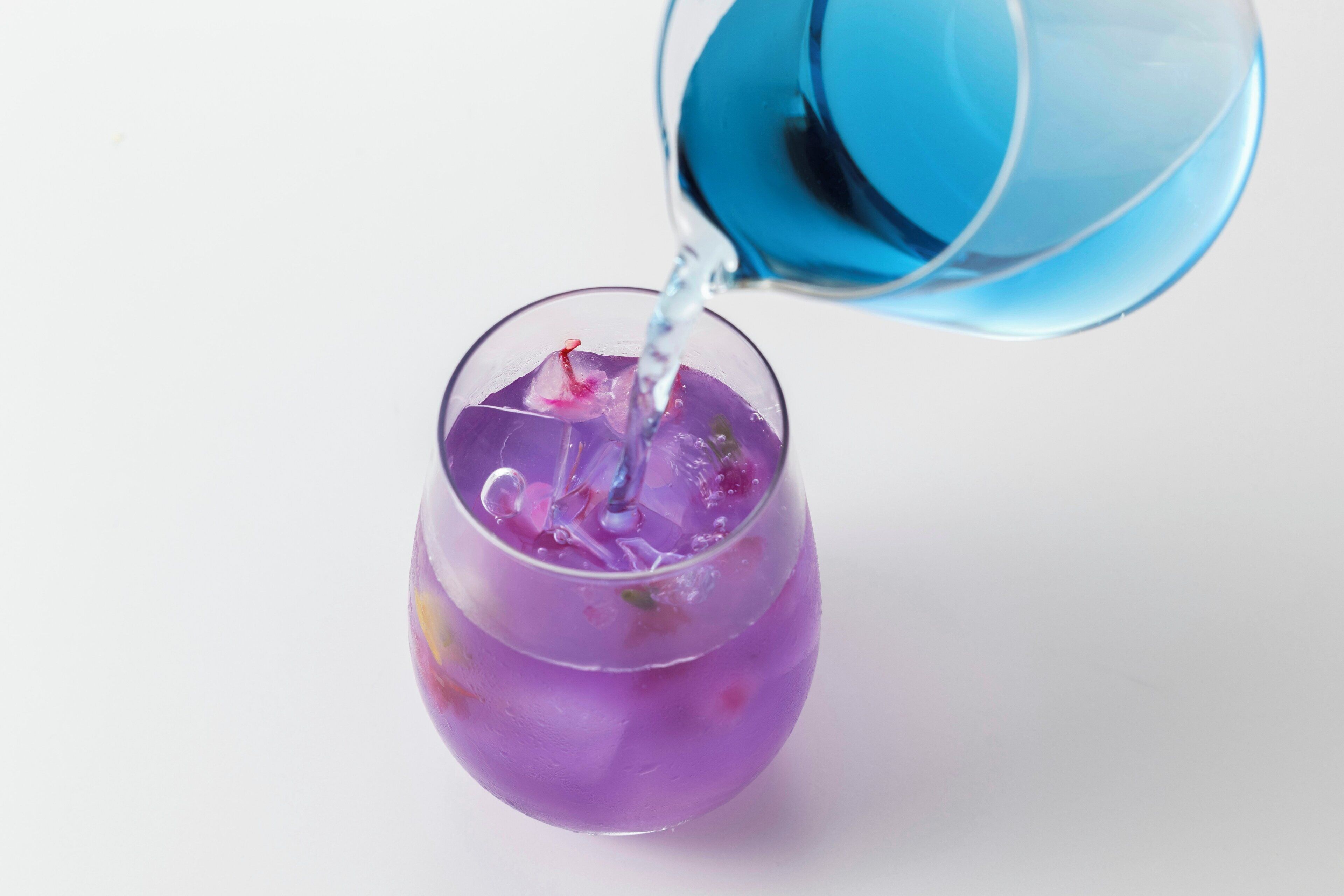 Een helder glas met een paars vocht en ijsblokjes, dat wordt gevuld met een blauw vocht.