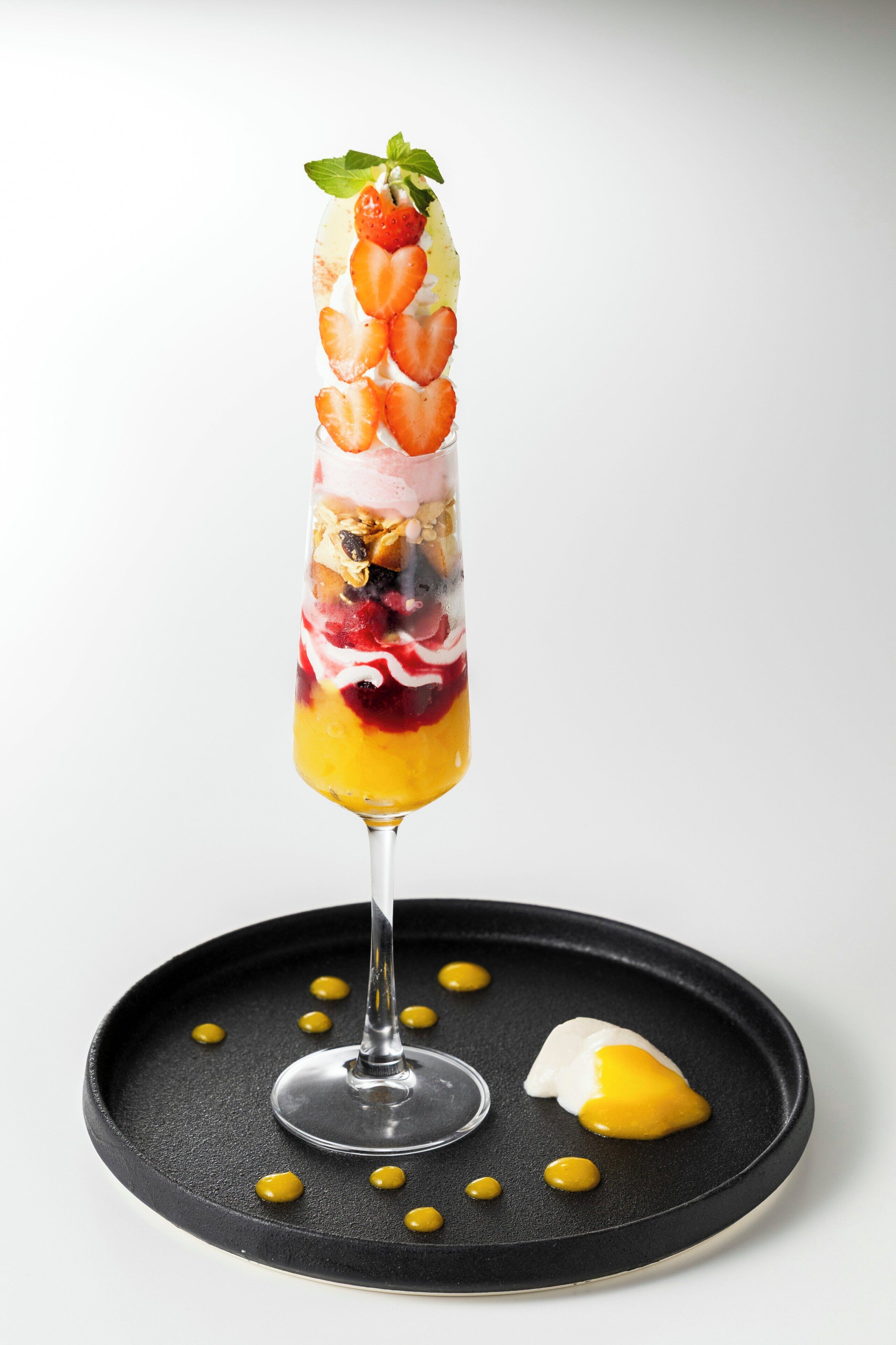 A dessert in a tall glass with layers of fruit, yogurt, and granola.