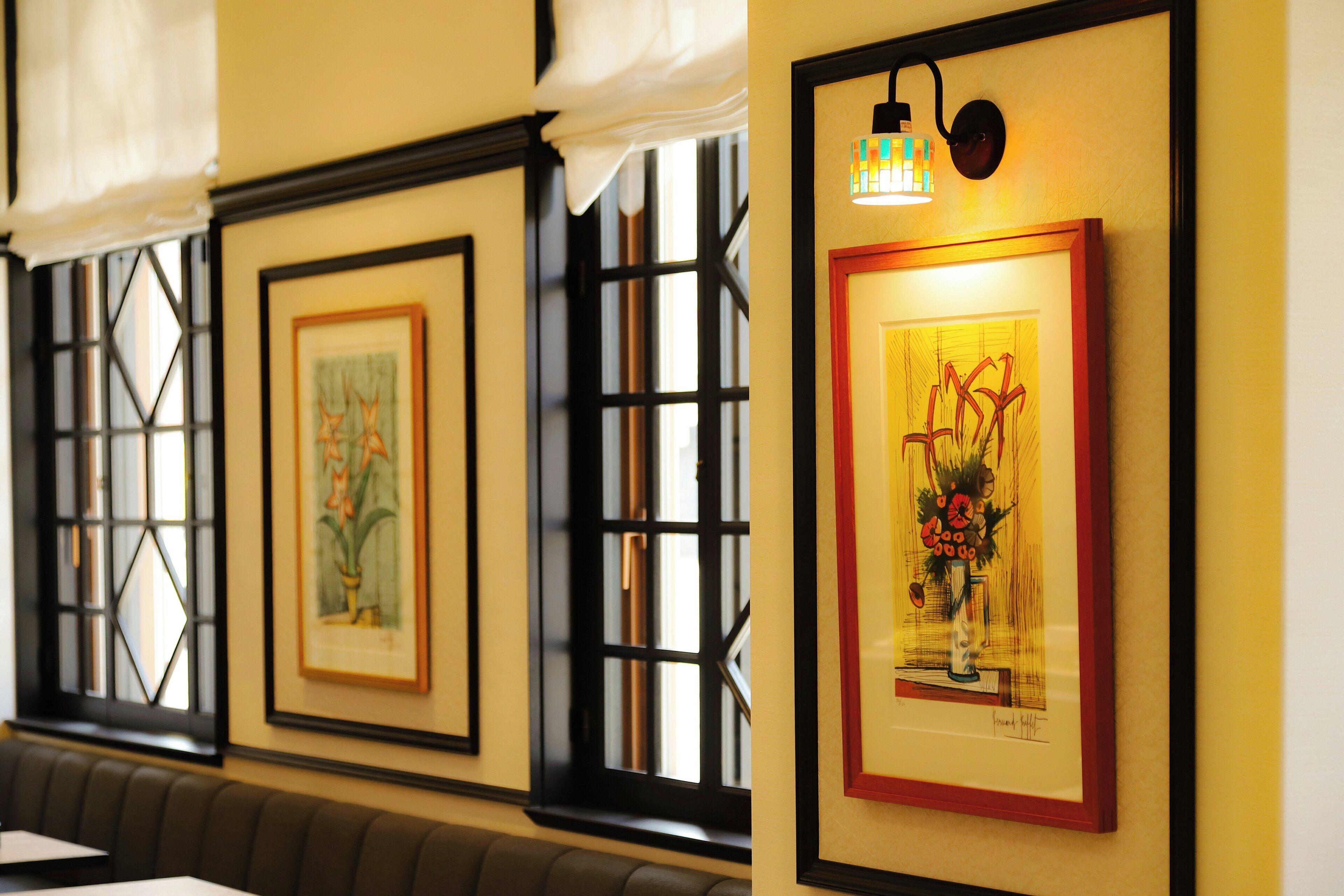 Framed artwork on a wall, a window with a view, and a bench.