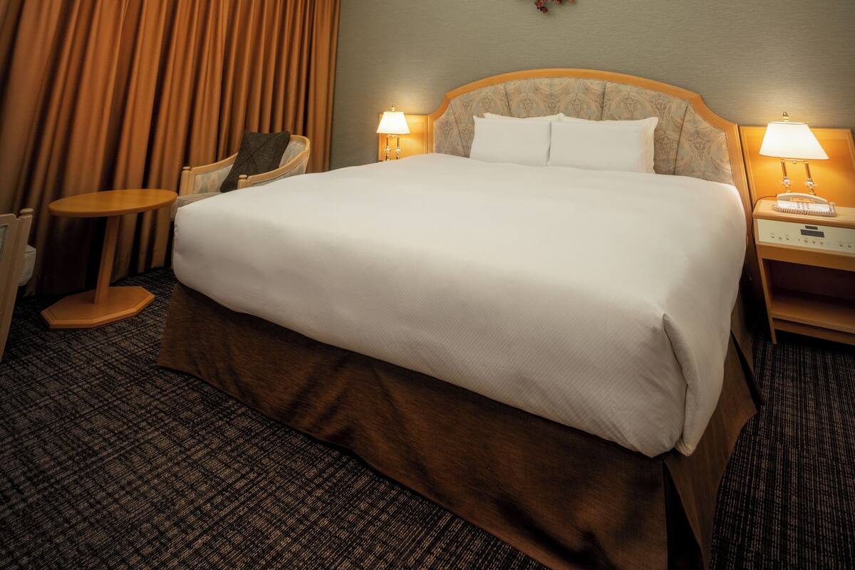 A hotel room with a large bed, two bedside tables with lamps, a ceiling fan, and a chandelier.