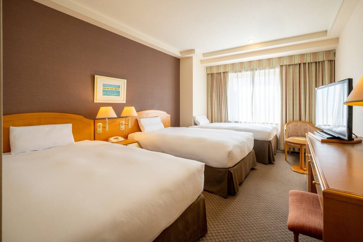 A hotel room with two beds, a desk, a chair, and a television.