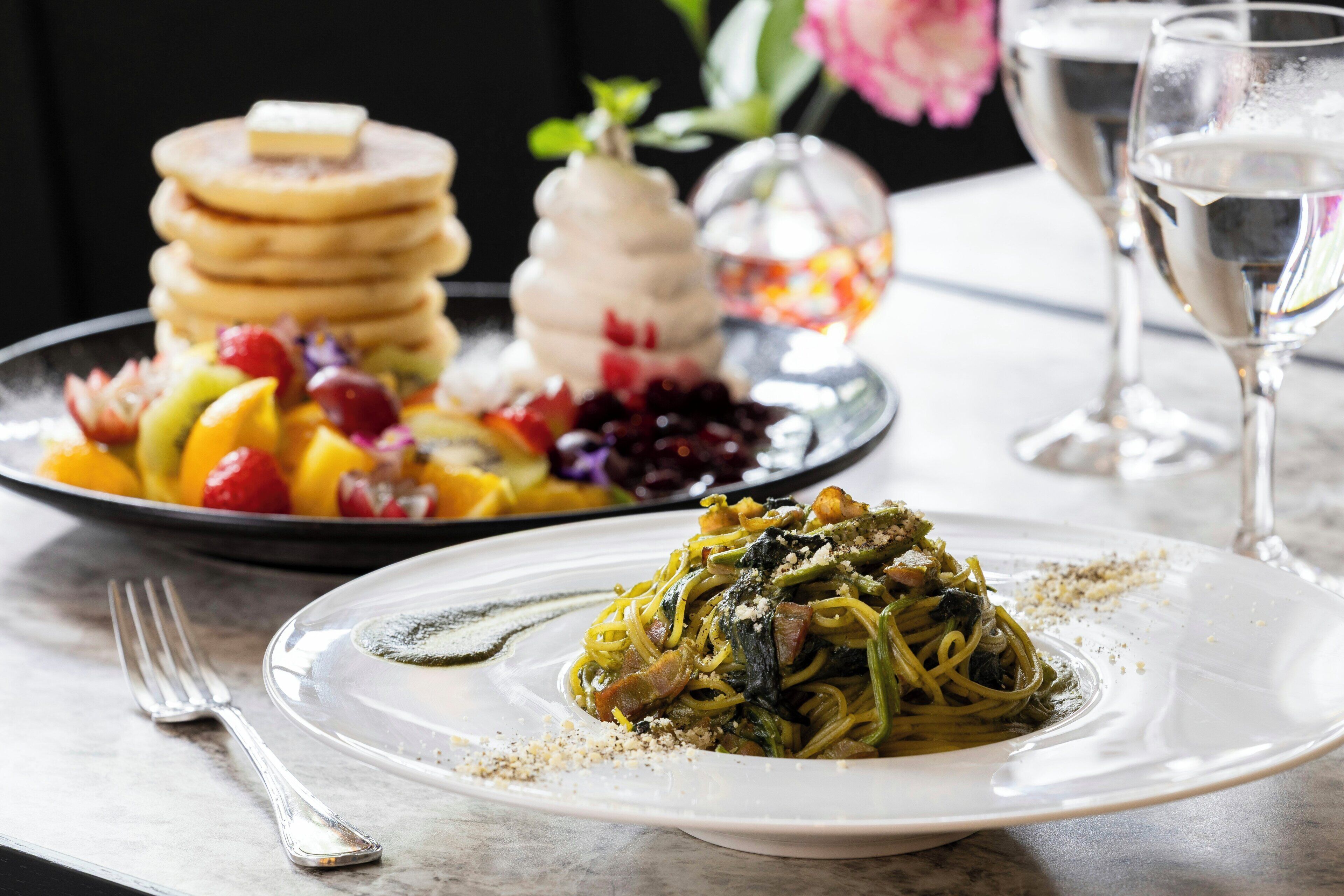 Un piatto di pasta con verdure e un bicchiere di vino bianco su un tavolo.