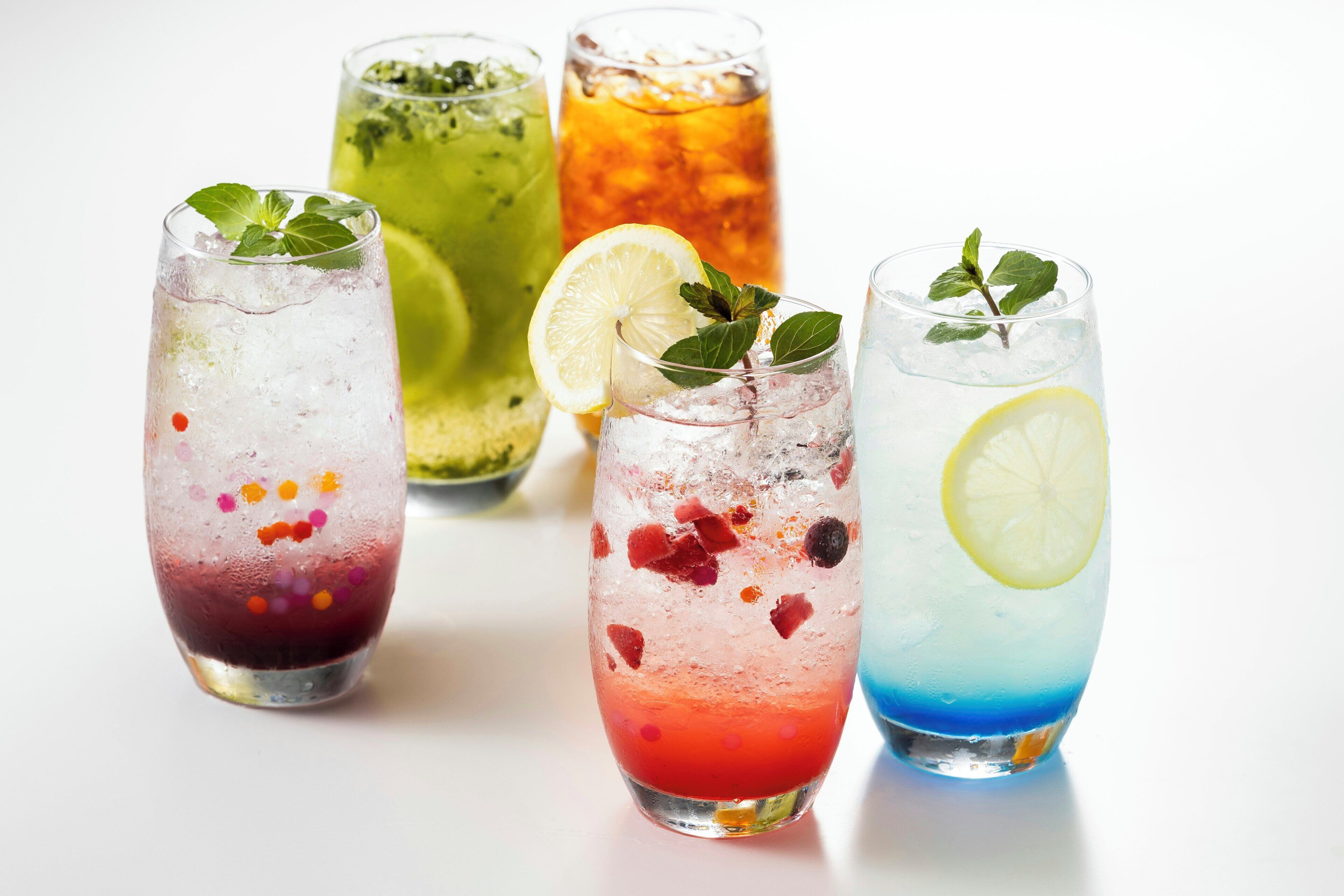 Four glasses of iced beverages with various fruits and mint leaves.