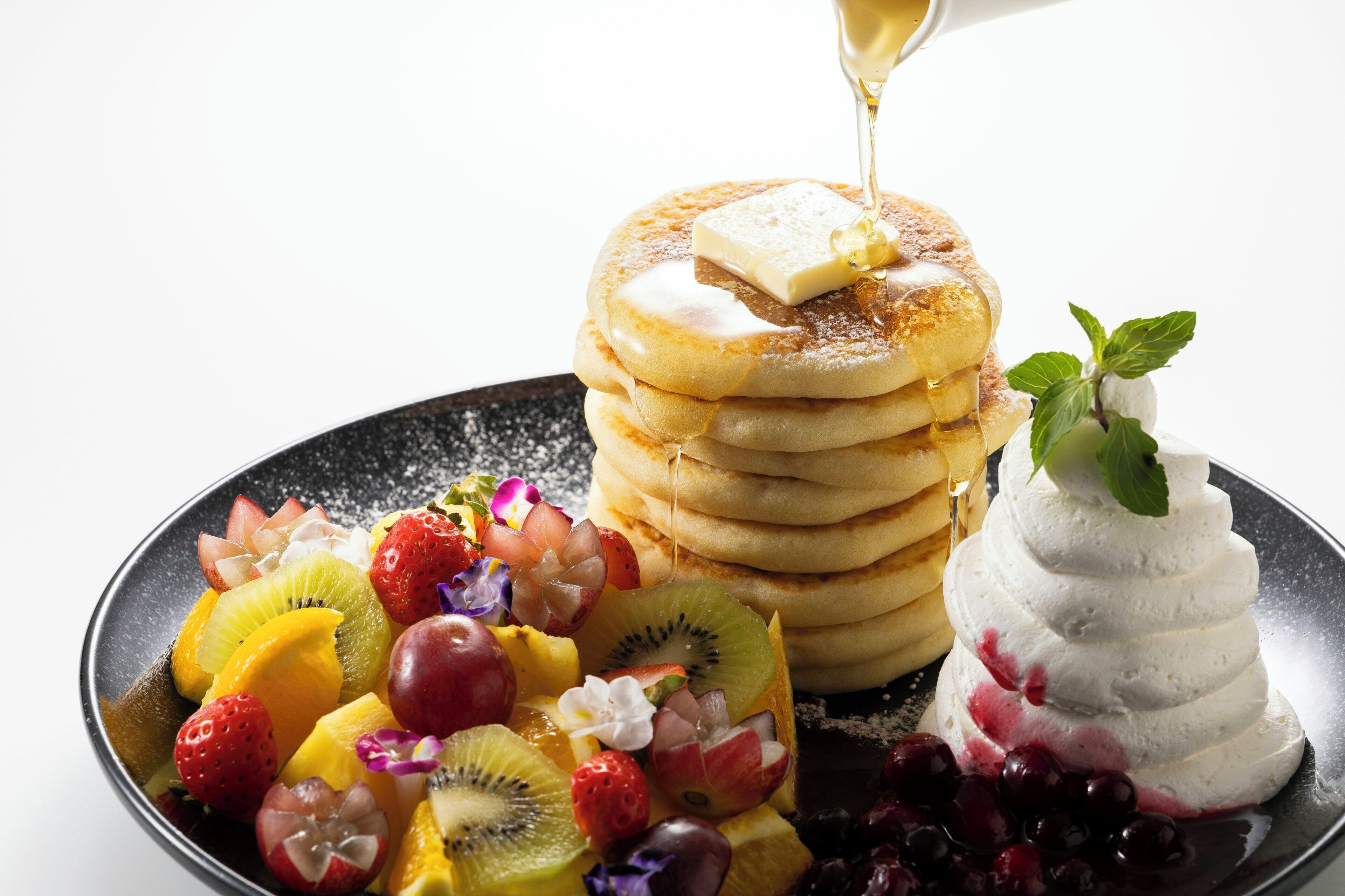 A stack of pancakes with syrup and a side of fruit.