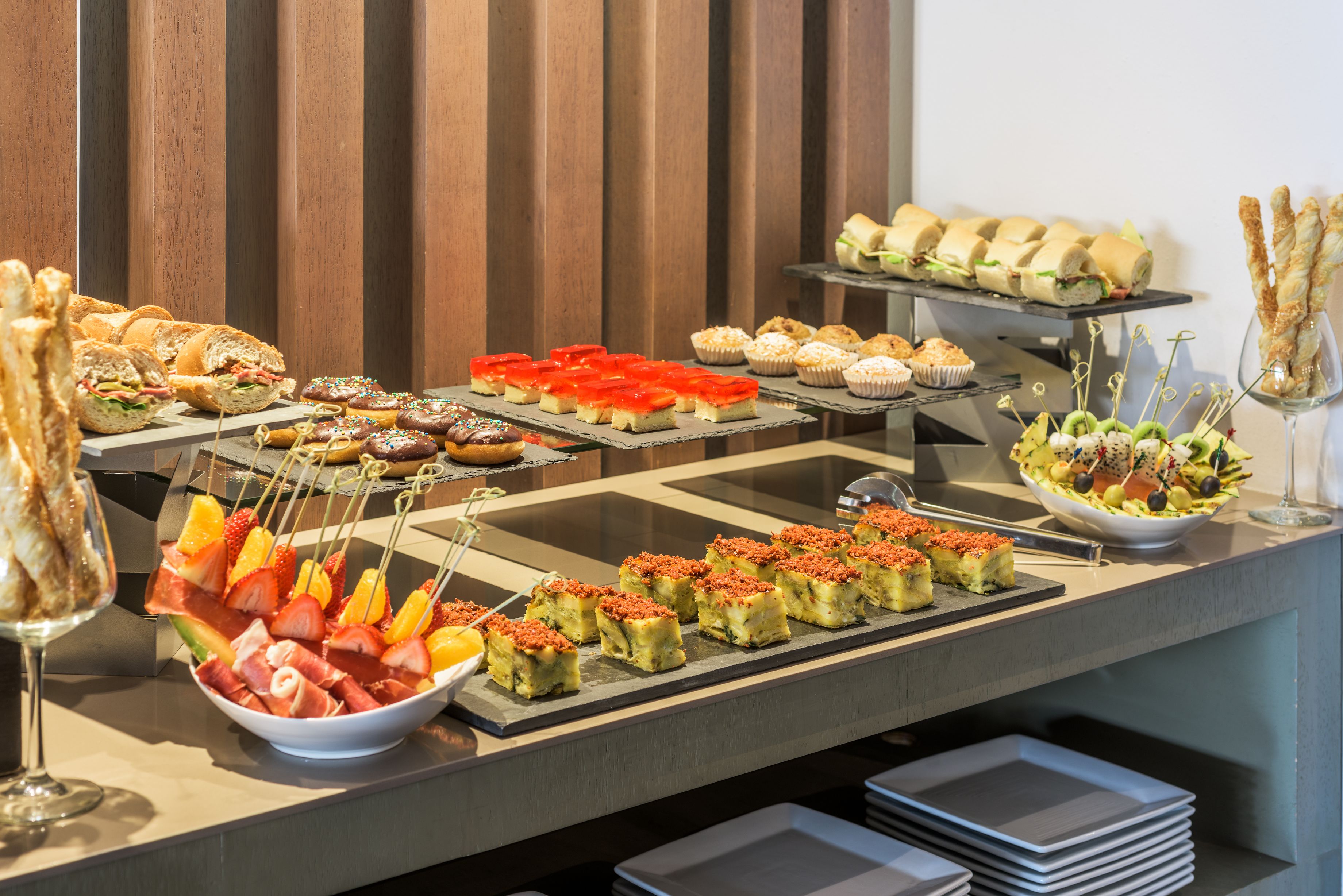Un bufé con diversas opciones de comida, incluyendo sándwiches, pasteles y brochetas de fruta.