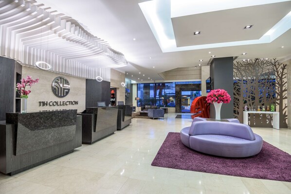 A modern reception area with a reception desk labeled "11th Collection," a purple seating area, and a decorative tree-like partition. - NH Collection Quito Royal (Quito)