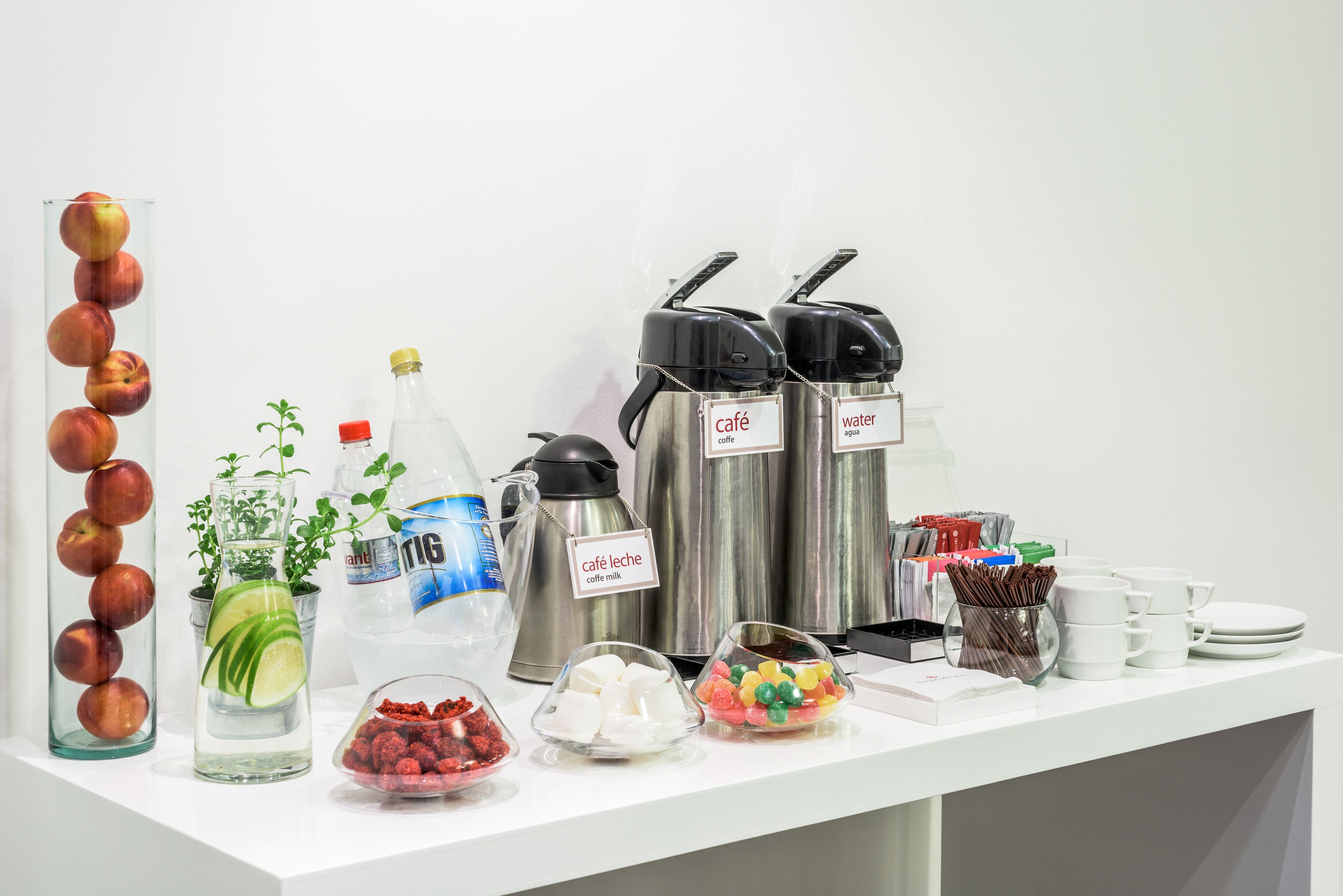 En drikkebuffet med forskellige automater, et glas med æbler og beholdere med snacks.