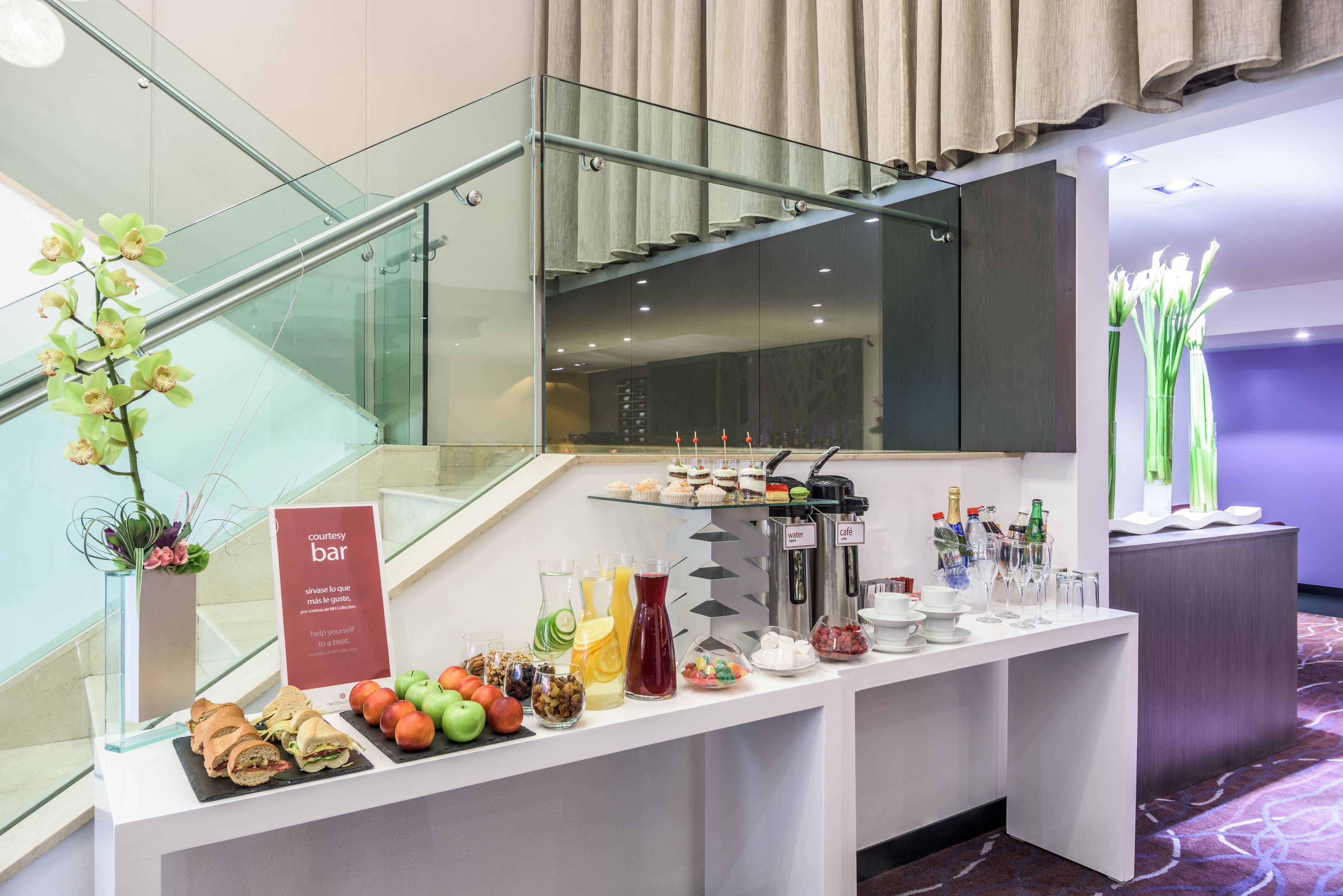 Montaje tipo bufé con diversos alimentos y bebidas, una barandilla de vidrio y una escalera.