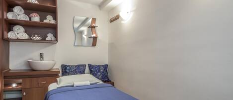A bedroom with a bed, a wooden dresser, a mirror, and a shelf with towels.