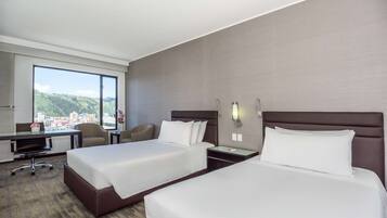Habitación de hotel con dos camas, un escritorio, una silla y un ventanal con vistas a la ciudad.
