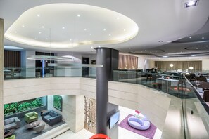 A modern hotel lobby with a glass railing, seating areas, and a large digital display. - NH Collection Quito Royal (Quito)